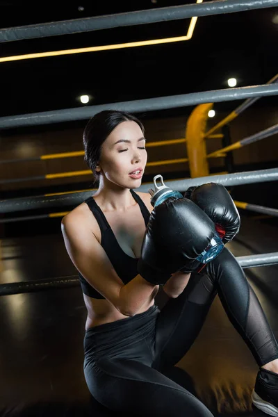 Attraente donna con gli occhi chiusi in possesso di bottiglia di sport mentre indossa guanti da boxe — Foto stock