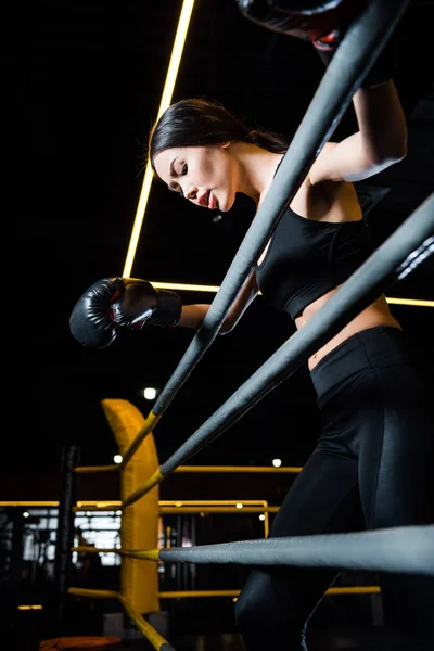 Низкий угол зрения спортивной женщины в боксёрских перчатках, стоящих в спортзале — стоковое фото