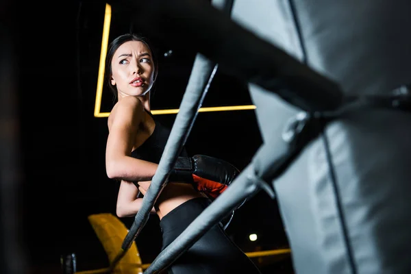 Vista de ángulo bajo de mujer atractiva en guantes de boxeo de pie en el gimnasio - foto de stock