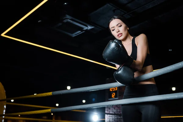 Низкий угол зрения расстроенной женщины, смотрящей на боксерские перчатки, стоя в спортзале — стоковое фото