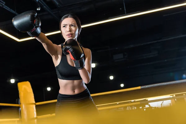 Selective focus of confident woman boxing while standing in boxing gloves in gym — Stock Photo