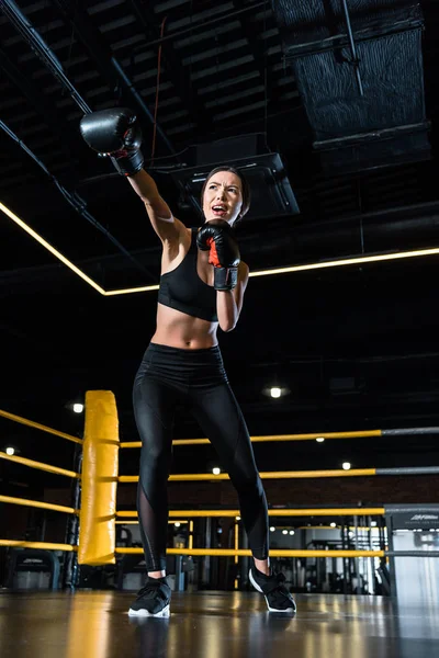 Low angle view of confident woman boxing while standing in boxing gloves in gym — Stock Photo