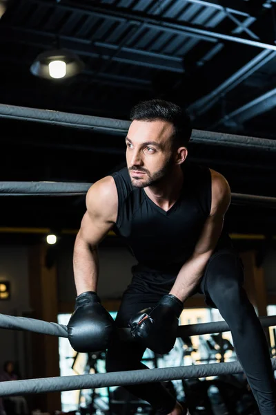 Handsome athletic man in boxing gloves standing near ropes in boxing ring — Stock Photo