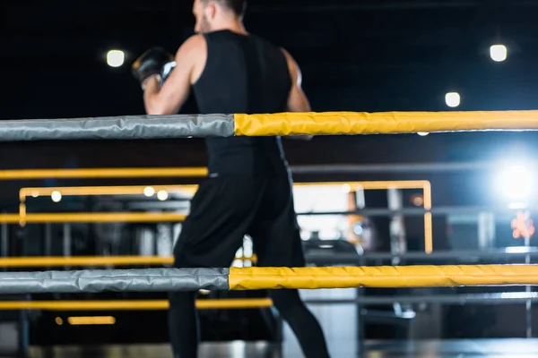 Селективный фокус боксёрского ринга с веревками рядом с атлетичным человеком, тренирующимся в боксёрских перчатках — стоковое фото