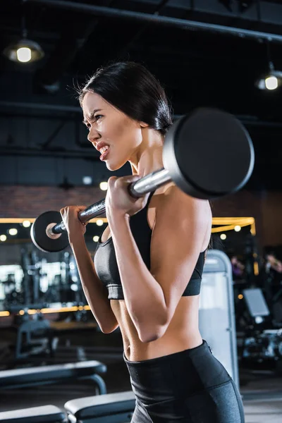 Vue à faible angle de la jeune femme faisant de l'exercice avec haltère lourde dans la salle de gym — Photo de stock