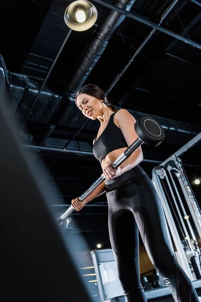 Visão de baixo ângulo de forte jovem mulher exercitando-se com barra pesada no ginásio — Fotografia de Stock