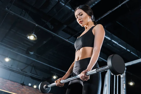 Tiefansicht attraktiver junger Frau beim Training mit schwerer Langhantel im Fitnessstudio — Stockfoto