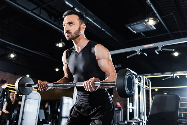 Vista a basso angolo dell'uomo atletico che esercita con pesante bilanciere in palestra — Foto stock