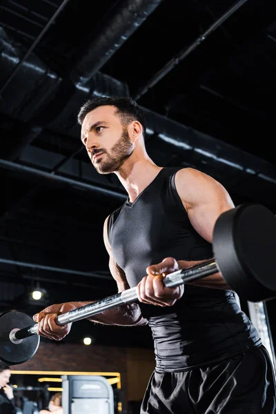 Vue à faible angle de l'homme athlétique travaillant avec haltère lourd dans la salle de gym — Photo de stock