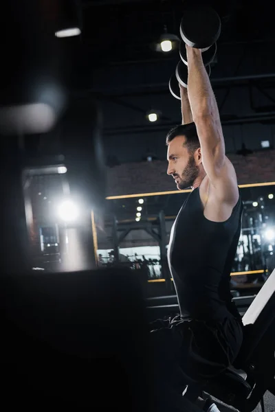 Selektiver Fokus eines gut aussehenden, athletischen Mannes, der im Fitnessstudio mit Hanteln trainiert — Stockfoto