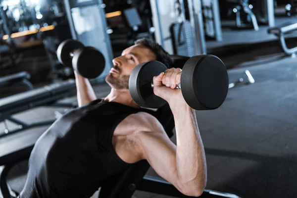 Enfoque selectivo del hombre barbudo haciendo ejercicio con pesas en el gimnasio - foto de stock