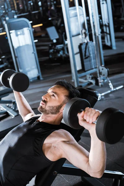 Selective focus of strong bearded man working out with dumbbells in gym — Stock Photo