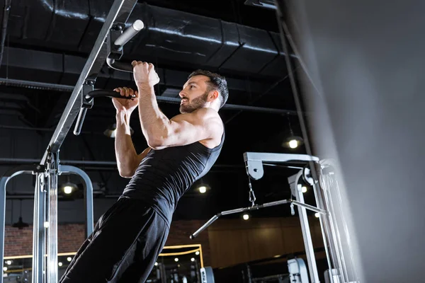 Low angle view of handsome man doing pull up in sports center — Stock Photo