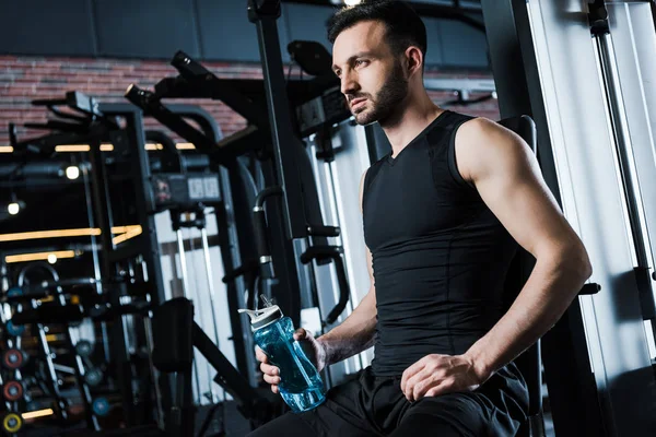 Vista de ángulo bajo del deportista guapo en ropa deportiva celebración de la botella de deporte en el gimnasio - foto de stock