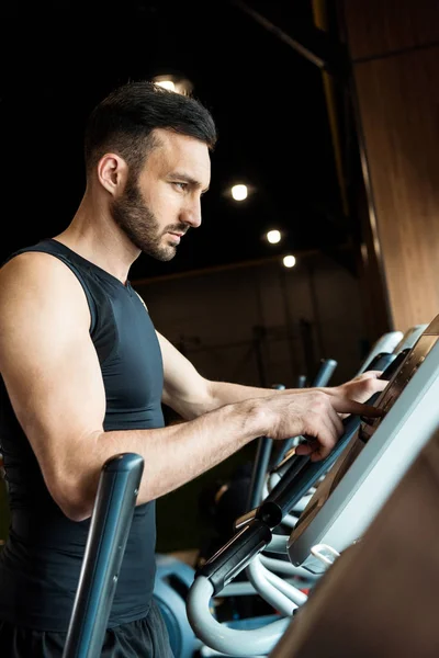 Selective focus of handsome athletic man pointing with finger while standing near exercise bikes — Stock Photo