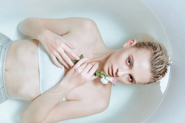Blick von oben auf zarte Frau, die sanft Blume in klarem Wasser in Badewanne hält — Stockfoto