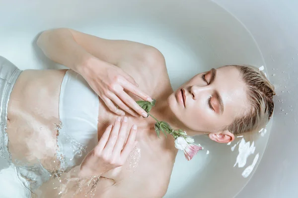 Vista dall'alto della donna sexy con gli occhi chiusi in acqua limpida nella vasca da bagno con fiore — Foto stock