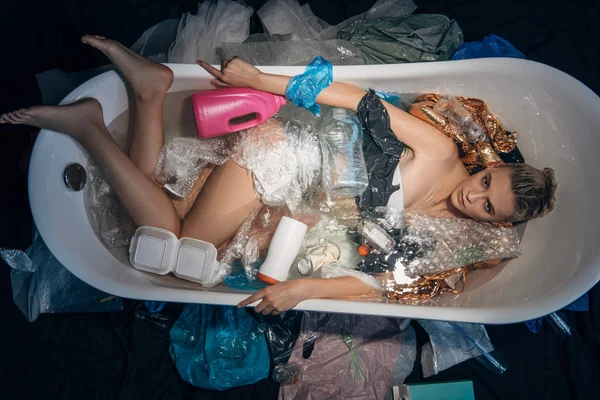 Вид зверху на молоду жінку, що плаває у ванні з пластиковим сміттям, концепція забруднення навколишнього середовища — стокове фото
