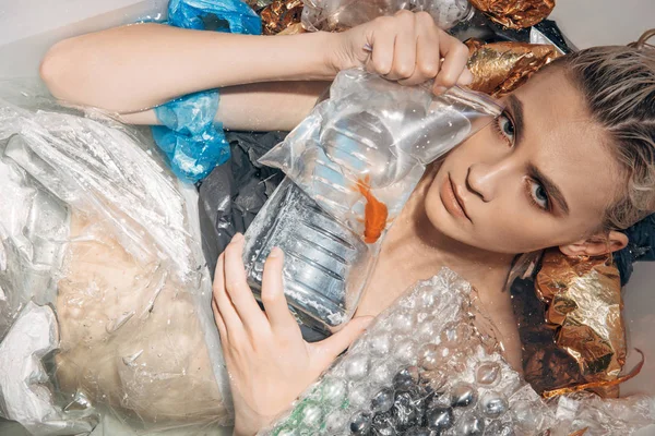 Sad wet woman holding goldfish in plastic bag among rubbish in bathtub — Stock Photo