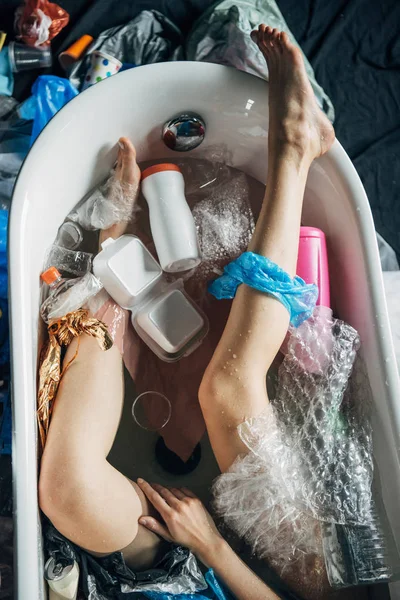 Vista dall'alto delle gambe femminili nella vasca da bagno con spazzatura, concetto di inquinamento ambientale — Foto stock
