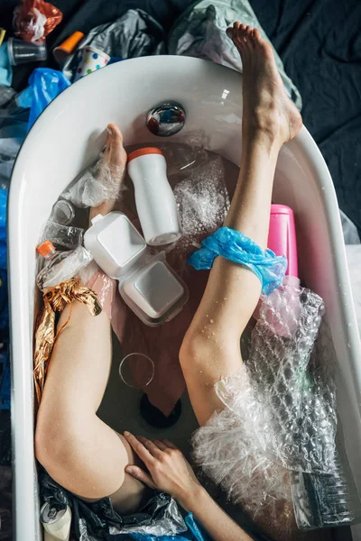Vista superior de las piernas femeninas en bañera con basura, concepto de contaminación ambiental — Stock Photo