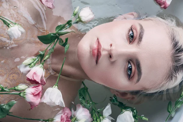 Vista superior da bela mulher deitada em água clara entre as flores e olhando para a câmera — Fotografia de Stock
