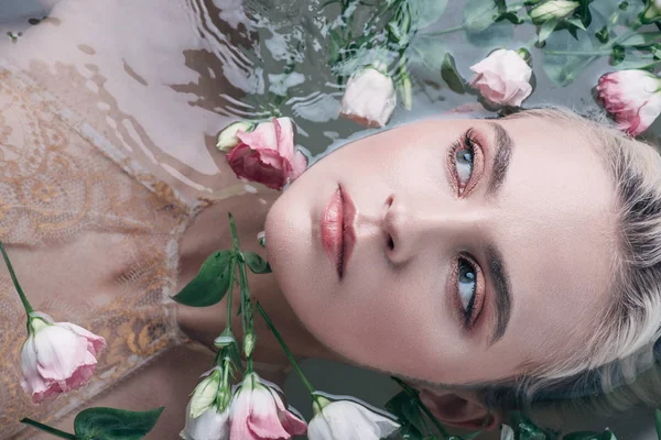 Vue de dessus de la belle femme couchée dans l'eau claire parmi les fleurs et regardant loin — Photo de stock