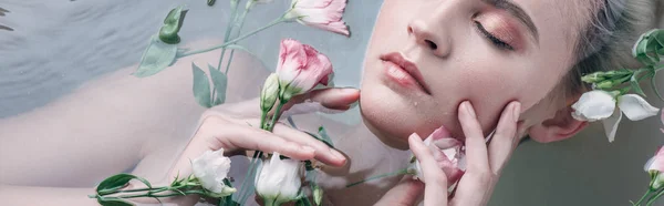 Draufsicht auf schöne Frau mit geschlossenen Augen, die in klarem Wasser mit Blumen liegt, Panoramaaufnahme — Stockfoto