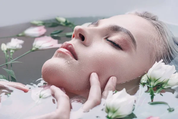 Schöne Frau mit geschlossenen Augen, die in klarem Wasser mit Blumen liegt — Stockfoto