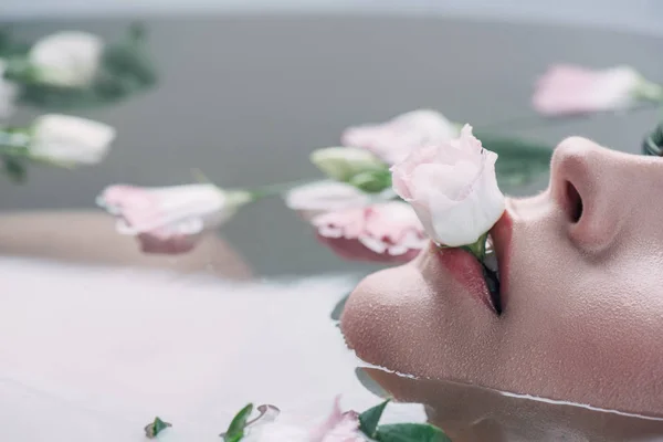 Vue partielle de belle femme couchée en eau claire avec rose dans la bouche — Photo de stock
