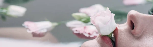 Vista ritagliata della donna sdraiata in acqua e tenuta rosa in bocca — Foto stock