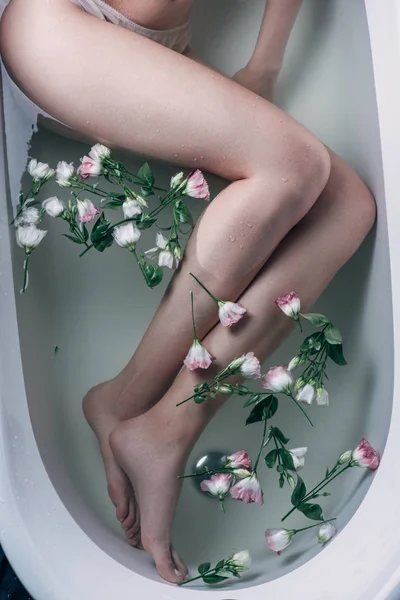 Vue de dessus de la femme couchée dans l'eau claire avec des fleurs dans la baignoire blanche — Photo de stock