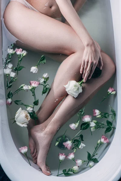 Вид зверху красивих жіночих ніг у чистій воді з квітами у білій ванні — стокове фото