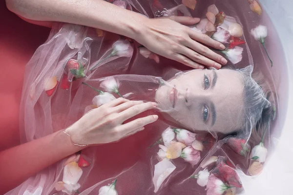 Vista dall'alto di bella donna ricoperta di tessuto a rete bianca in acqua rosa con fiori — Foto stock