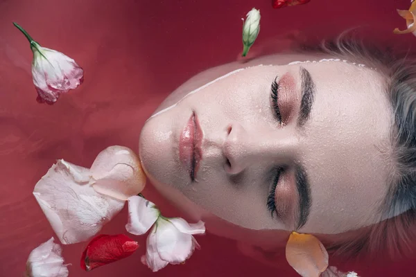 Вид сверху на красивую женщину с закрытыми глазами в розовой воде с лепестками роз — стоковое фото