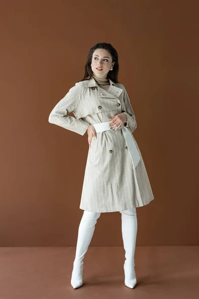 Mulher na moda em casaco elegante trincheira isolado em marrom com a mão no quadril — Fotografia de Stock