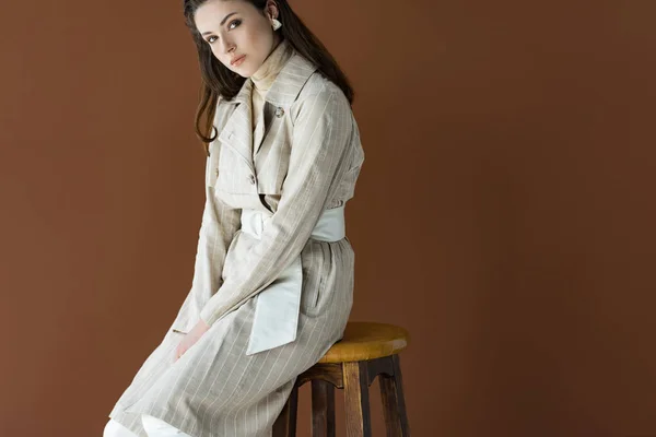 Mujer de moda sentada en silla aislada en marrón, mirando a la cámara - foto de stock