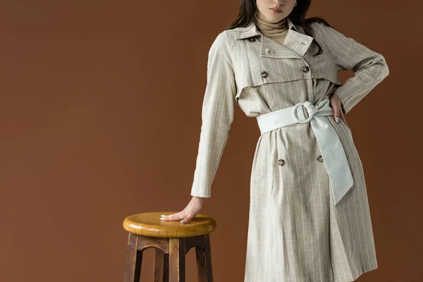 Vista cortada de mulher elegante em pé perto da cadeira isolada no marrom — Fotografia de Stock
