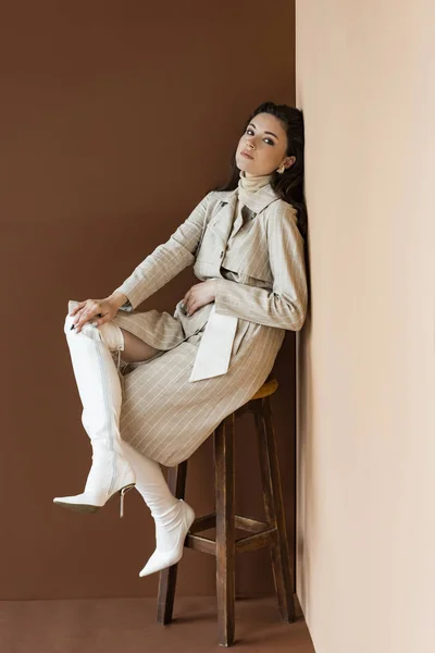 Femme à la mode en trench coat assis sur une chaise, regardant la caméra — Photo de stock