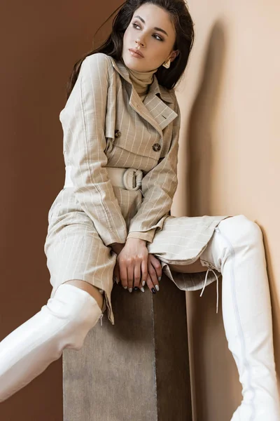 Vista de ángulo bajo de la mujer con estilo en la gabardina de moda sobre fondo marrón - foto de stock