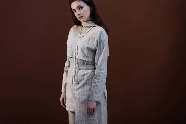 Modische Modell in stilvoller Kleidung auf braunem Hintergrund stehend, Blick in die Kamera — Stockfoto
