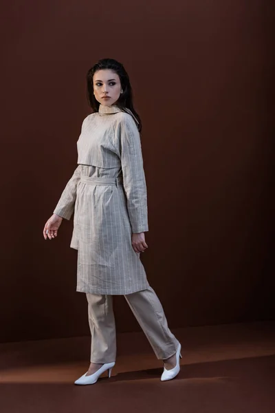Модна модель в стильному одязі та білому взутті, що йде на коричневому фоні — стокове фото
