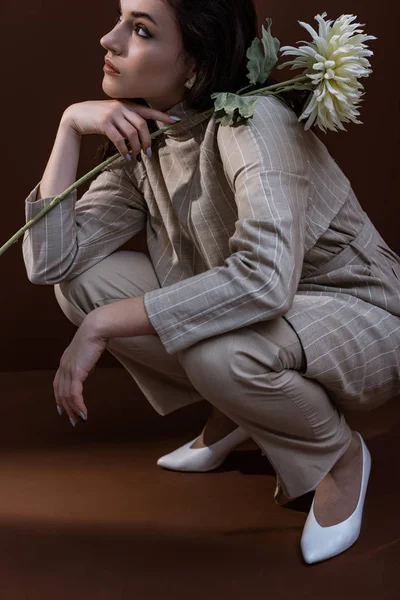 Взрослая женщина держит в руках белый хризантем, сидя на коричневом фоне — стоковое фото