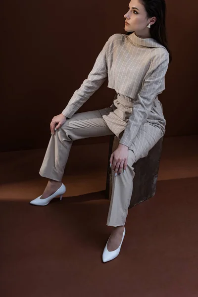 High angle view of beautiful and trendy woman sitting on box with brown background — Stock Photo