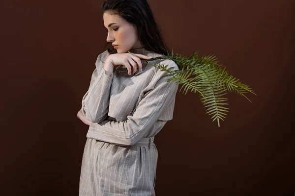 Trendy model closing eyes, holding fern leaves in hands, standing on brown background — Stock Photo