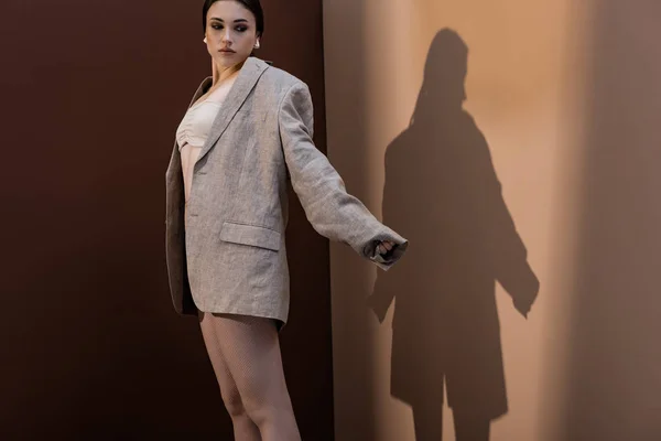 Mujer de moda en ropa interior y chaqueta de pie sobre fondo marrón, mirando hacia otro lado - foto de stock