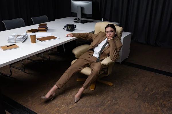Vista de ángulo alto de la exitosa y hermosa mujer de negocios sentada en el sillón en la oficina, mirando hacia otro lado - foto de stock