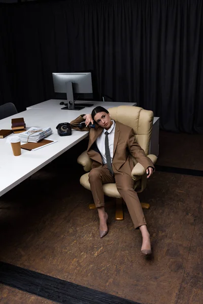 Vue grand angle de belle femme d'affaires avec combiné assis sur un fauteuil dans l'espace de travail de bureau, en regardant la caméra — Photo de stock