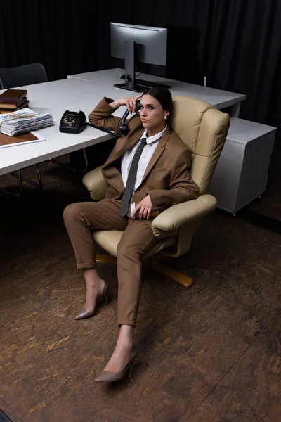 Vue grand angle de femme d'affaires avec combiné et tasse en papier assis sur un fauteuil dans le bureau, regardant la caméra — Photo de stock