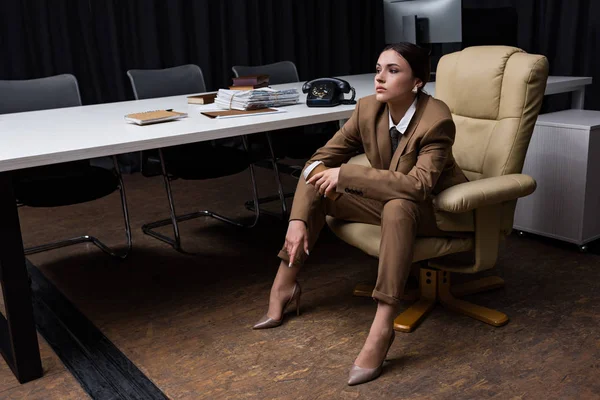 Fashionable businesswoman in suit sitting on armchair in office, looking away — Stock Photo